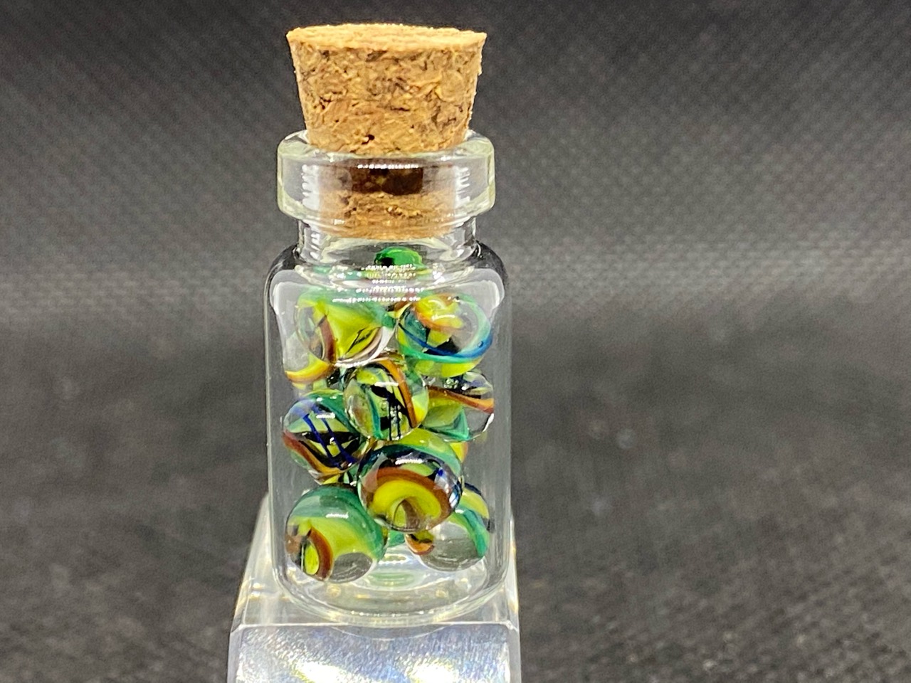 Lemon & Teal Ribbon Mini Micro Marbles: Corked miniature bottle filled with lemon-yellow and teal ribbon micro marbles on a clear block