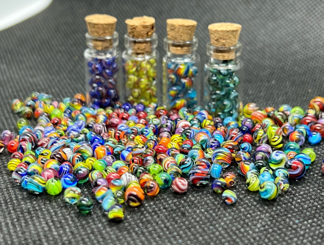 Micro Marble Color Collection: Wide angled display of four corked jars behind an array of striped and swirled micro marbles