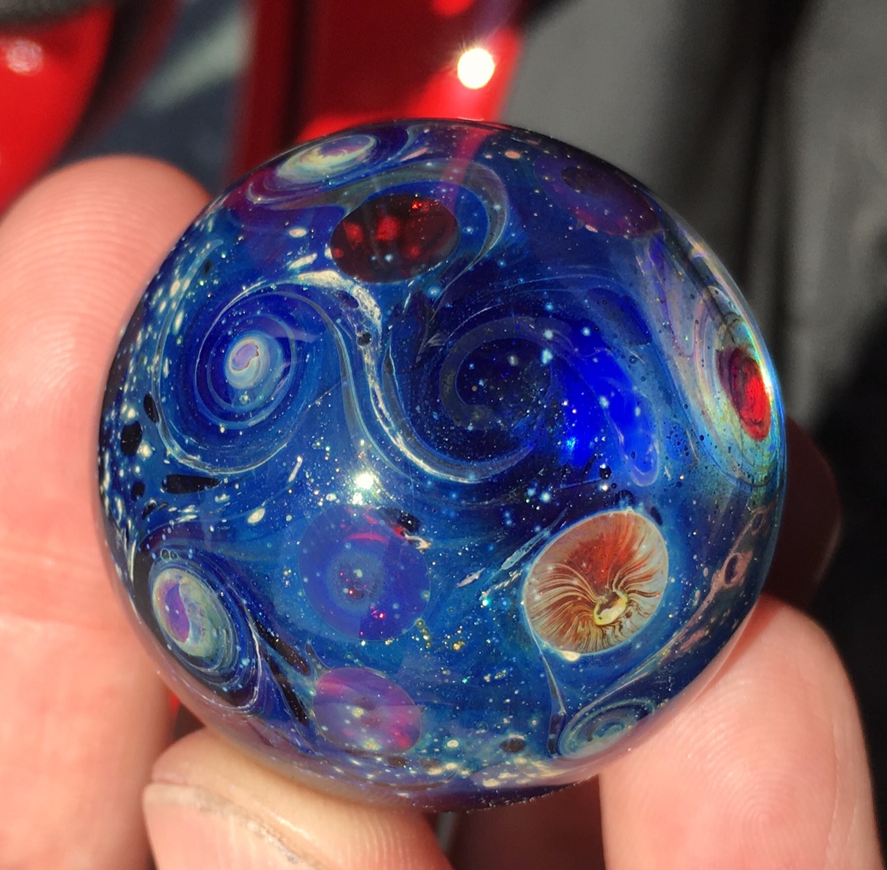 Milky Way Galaxy Space Marble: Sunlit close view of cobalt-blue depths, pale spiral galaxies and red, violet and amber planetary forms