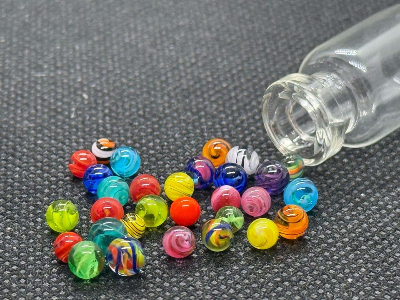 Close view of colorful ribbons and swirls in Mixed Colors Mini Micro Marbles beside their open jar