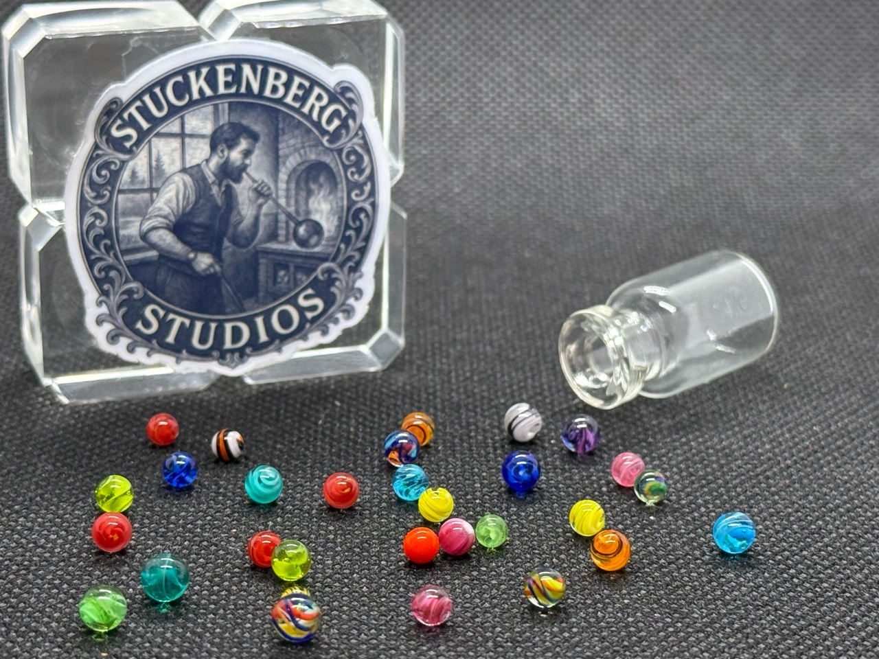 Loose Mixed Colors Mini Micro Marbles in bright colors beside their open jar and studio branding