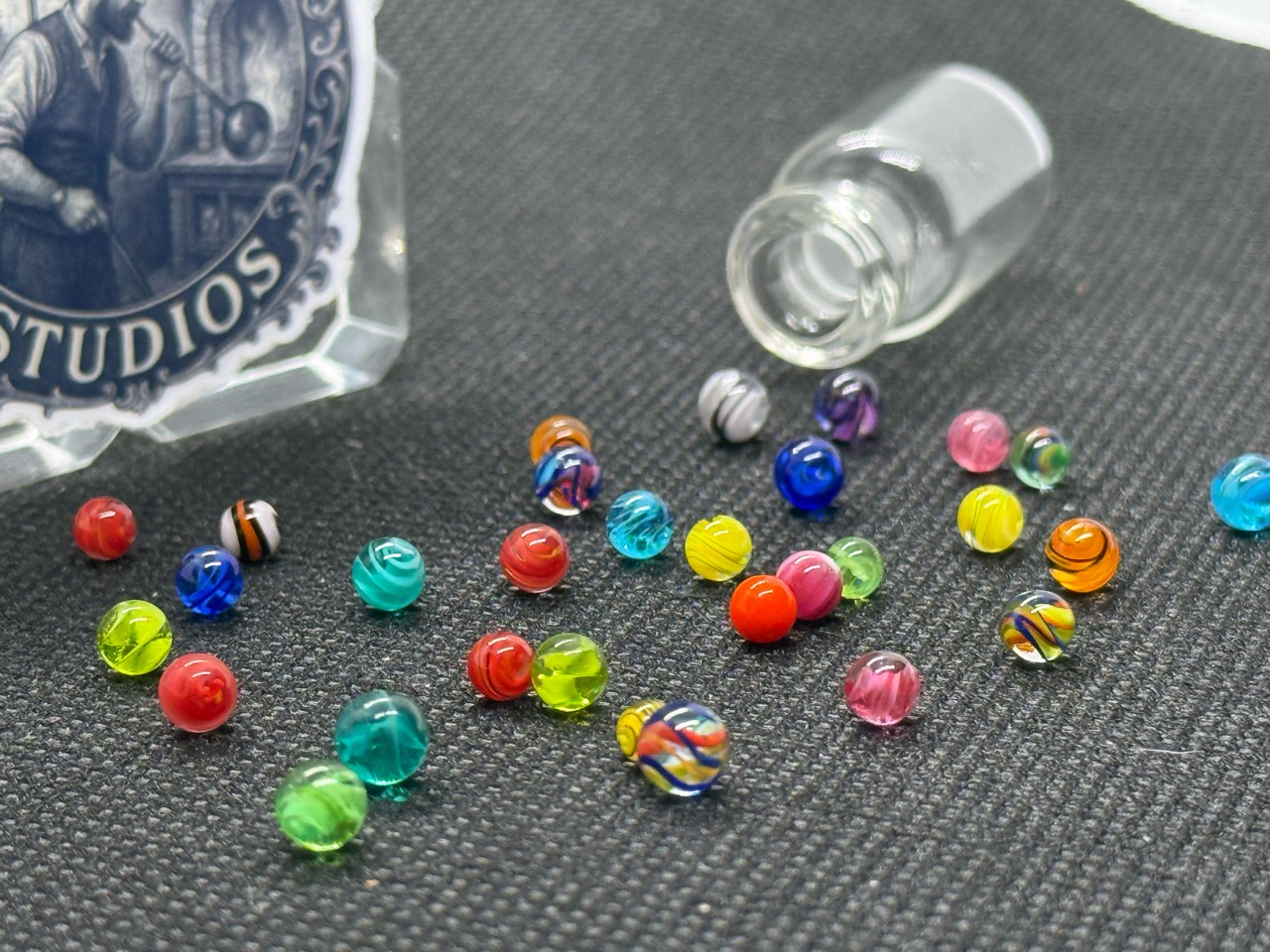 Mixed Colors Mini Micro Marbles spread beside their open jar, showing translucent colors and contrasting ribbons