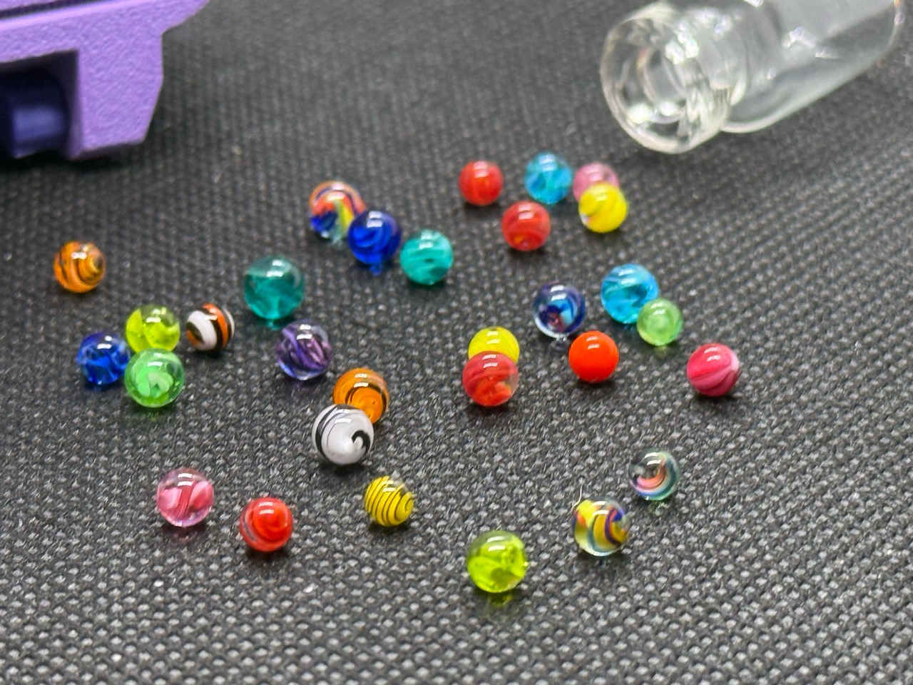 Mixed Colors Mini Micro Marbles with fine lines and colorful swirls below their lavender hard case