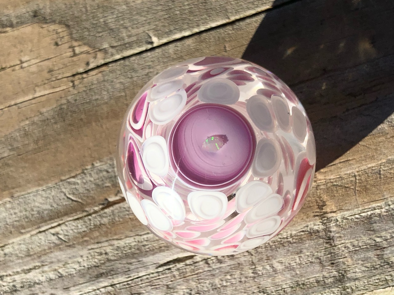 Opal Tentacle Dot Stack Marble: Sunlit full view of the opal centerpiece inside a pink cup surrounded by white and pink tentacle dot stacks