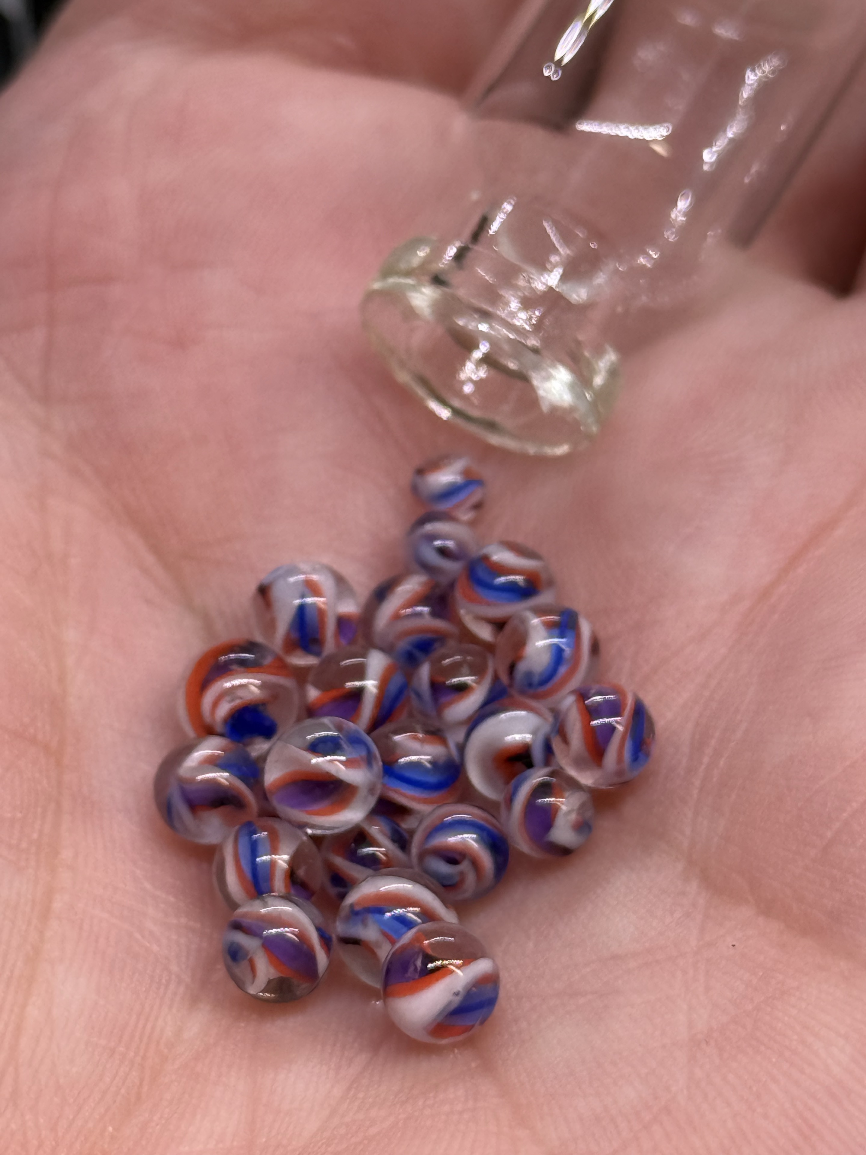 Pink Not Pink Mini Micro Marbles resting in a hand beside their glass jar