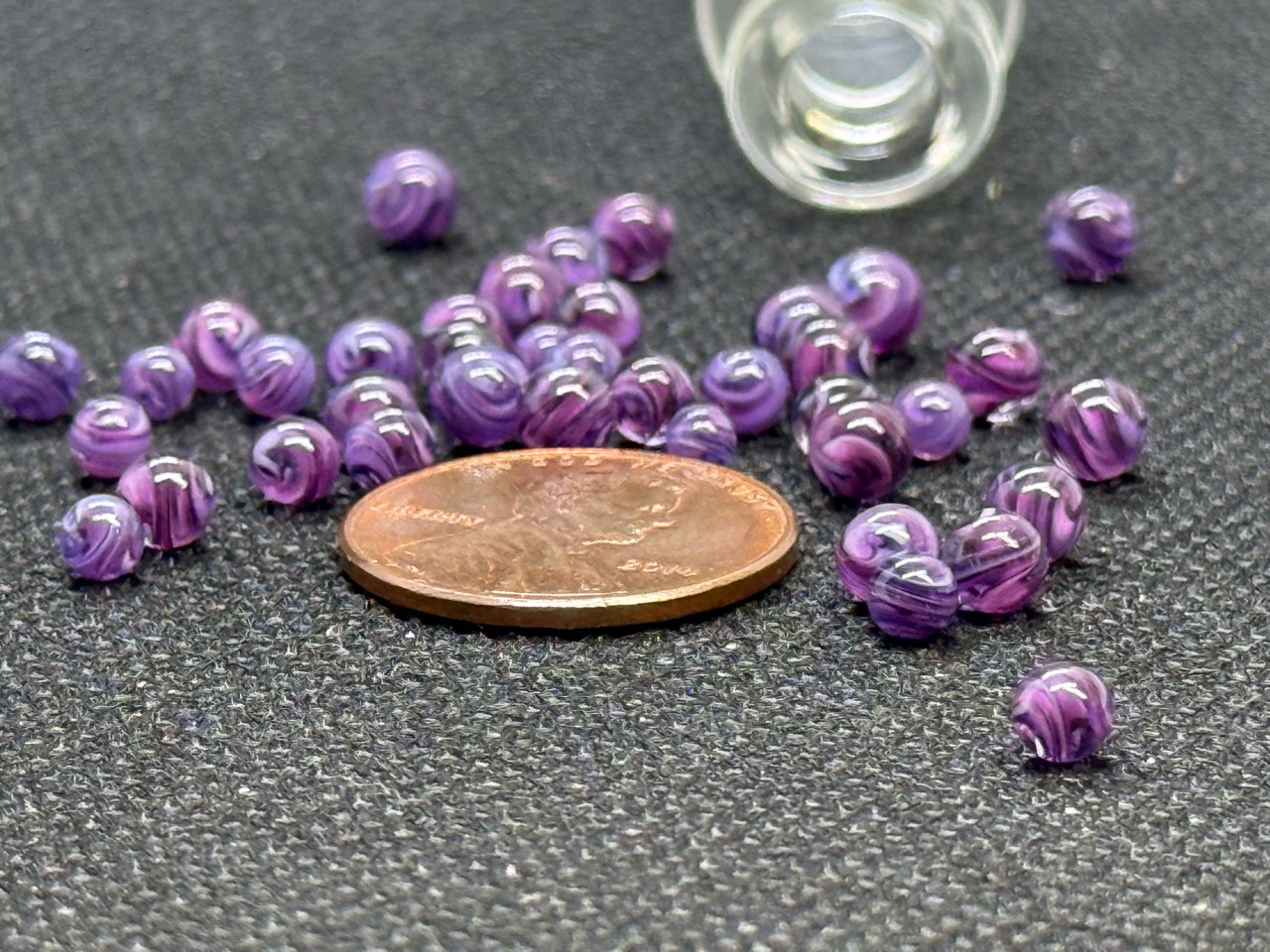 Purple Dream Mini Micro Marbles gathered around a penny for scale