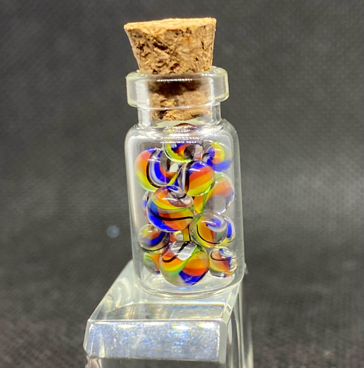 Rainbow Micro Marbles: Close bottle view of rainbow micro marbles with bright multicolored ribbons in clear glass