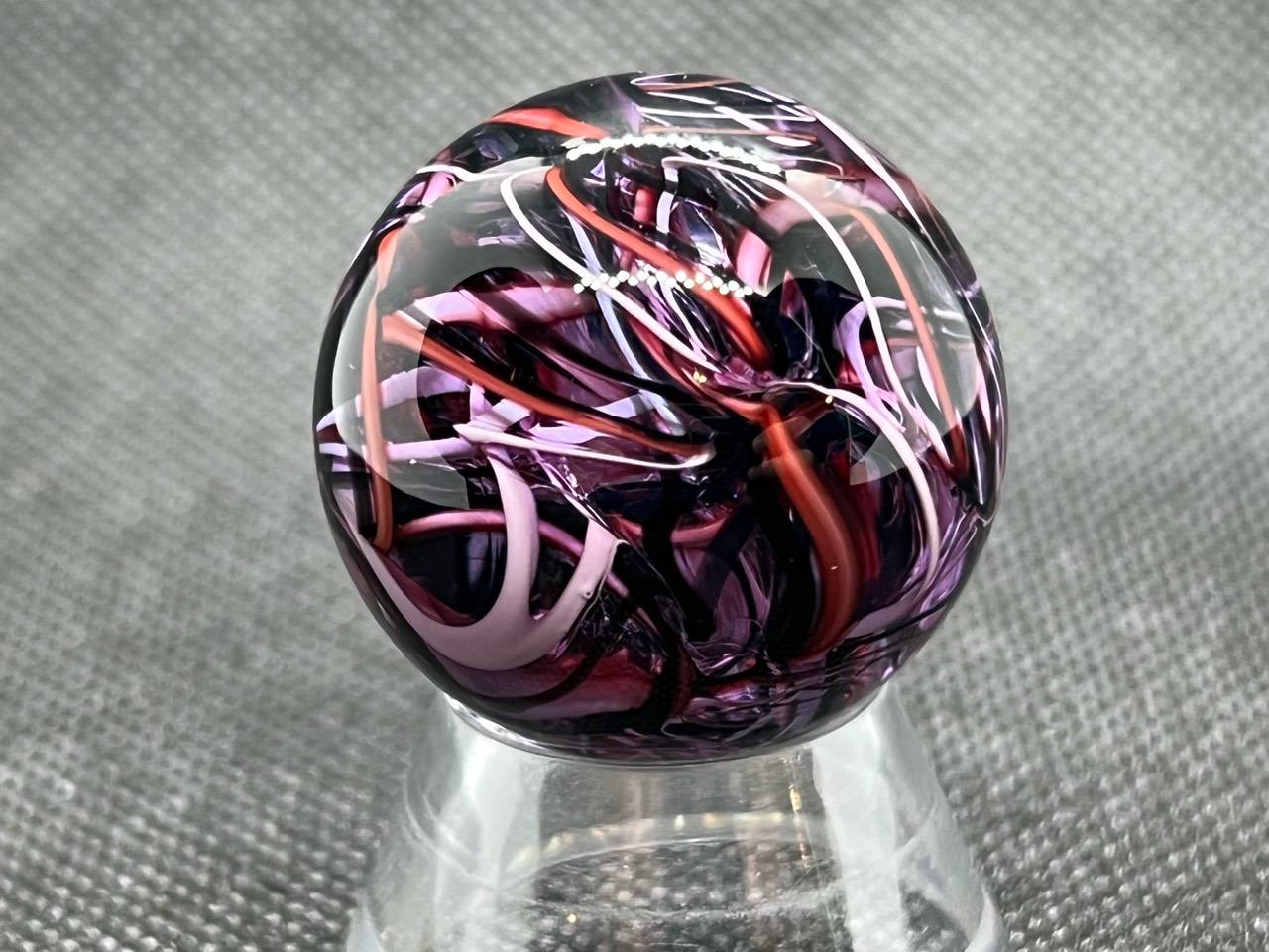 Rose & Lavender Ribbon Pocket Marble: Close view of pink, lavender and coral ribbons layered through dark plum glass
