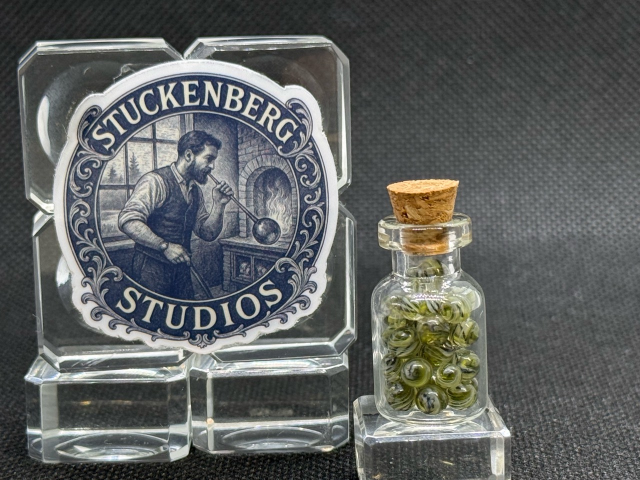 UV Champagne Mini Micro Marbles in their corked glass jar beside studio branding in ordinary light