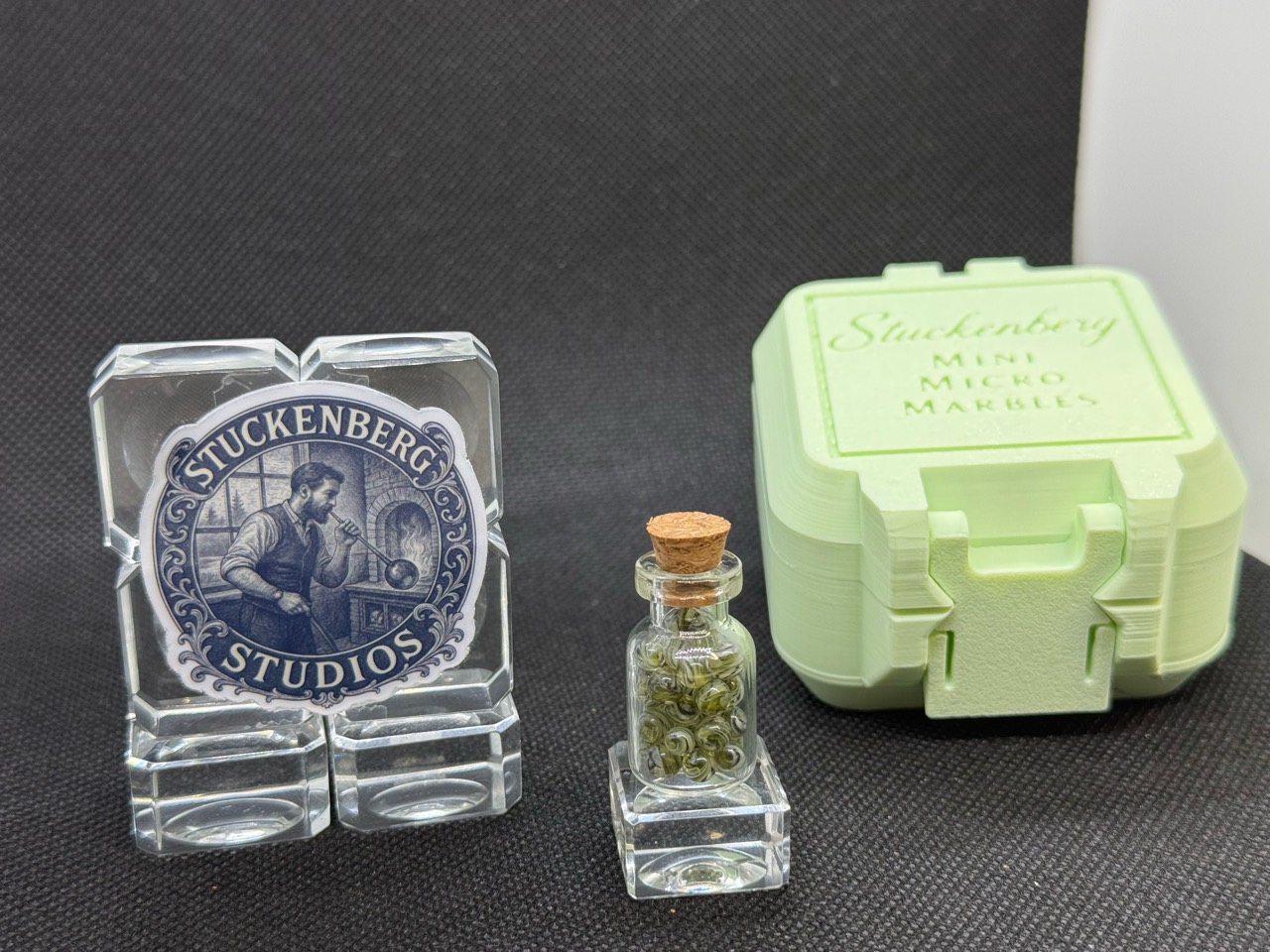 UV Champagne Mini Micro Marbles in their corked jar beside studio branding and a pale green hard case in ordinary light