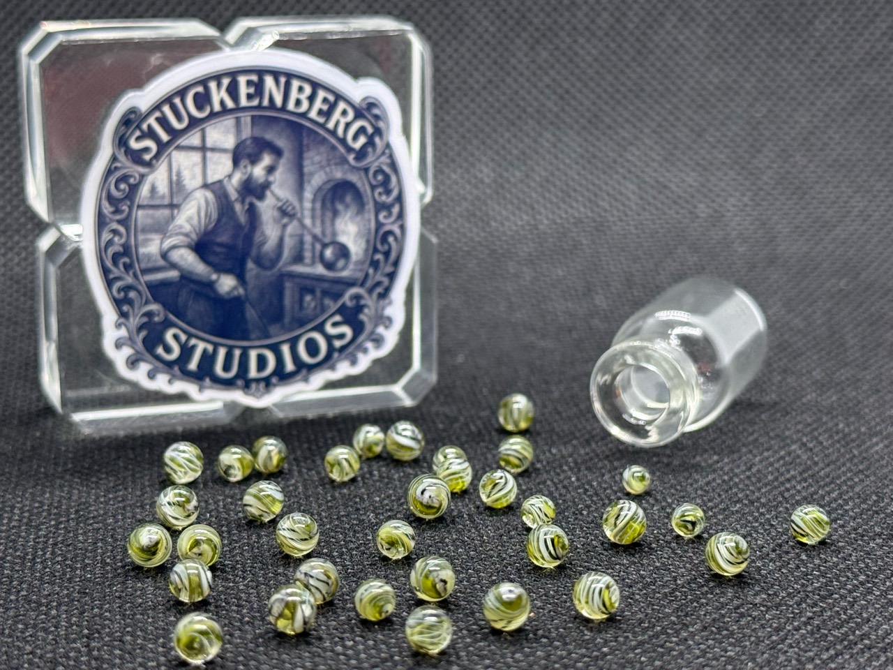 Loose UV Champagne Mini Micro Marbles with delicate fine lines beside their open jar in ordinary light