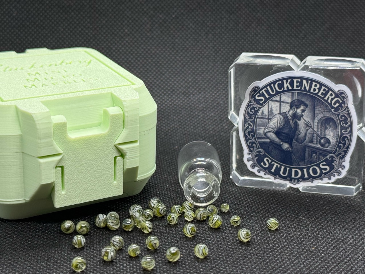 UV Champagne Mini Micro Marbles spread beside their open jar, studio branding and pale green hard case in ordinary light