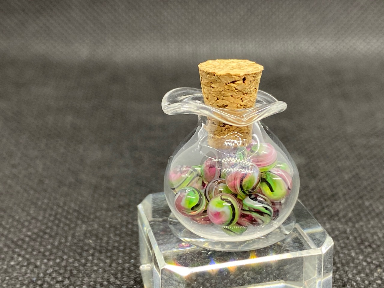Watermelon Mini Micro Marbles — 2021: corked glass jar of pink and green mini micro marbles on a clear stand
